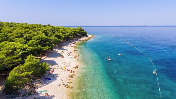 A beach with clear turquoise water, a sandy shore, and dense green trees. - Camp Adriatik (Primosten)