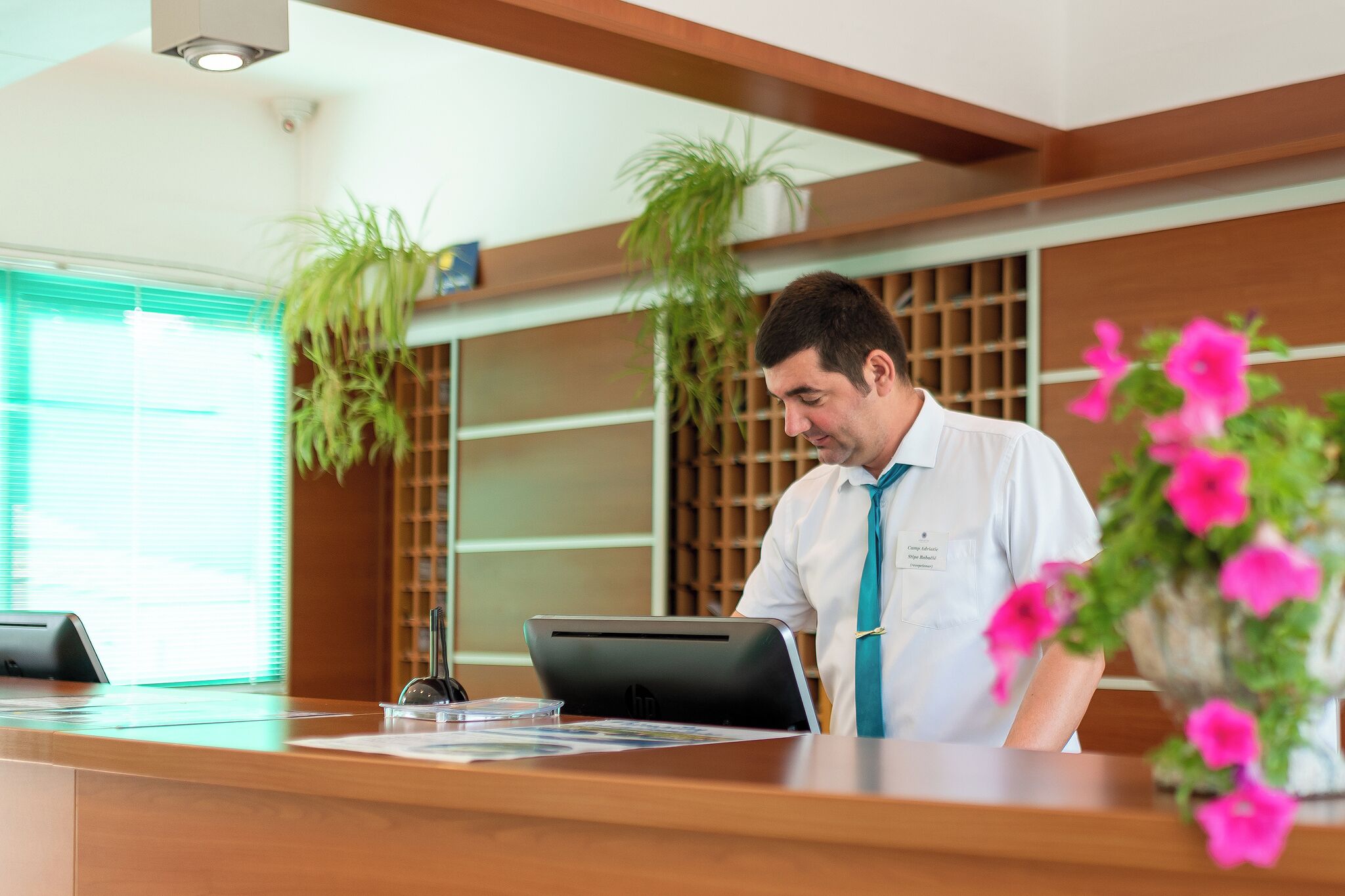 Un comptoir d’accueil avec un ordinateur portable, une plante et un vase de fleurs.