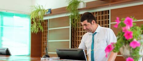 A reception desk with a laptop, a plant, and a vase of flowers.