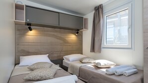 A hotel room with two beds, a built-in TV, and a window with curtains. - Camp Adriatik (Primosten)