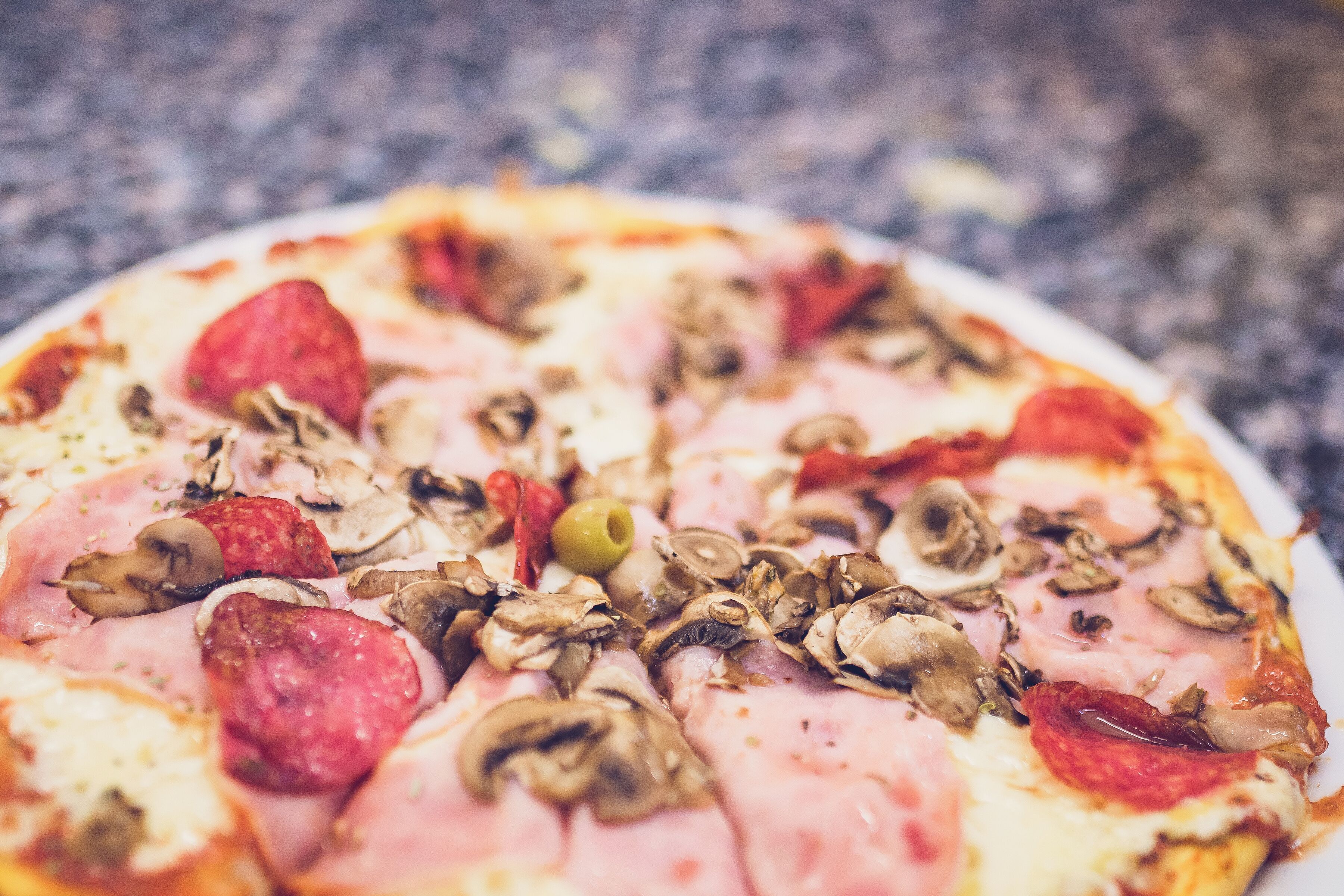 A pizza with pepperoni, mushrooms, and ham on a white plate.