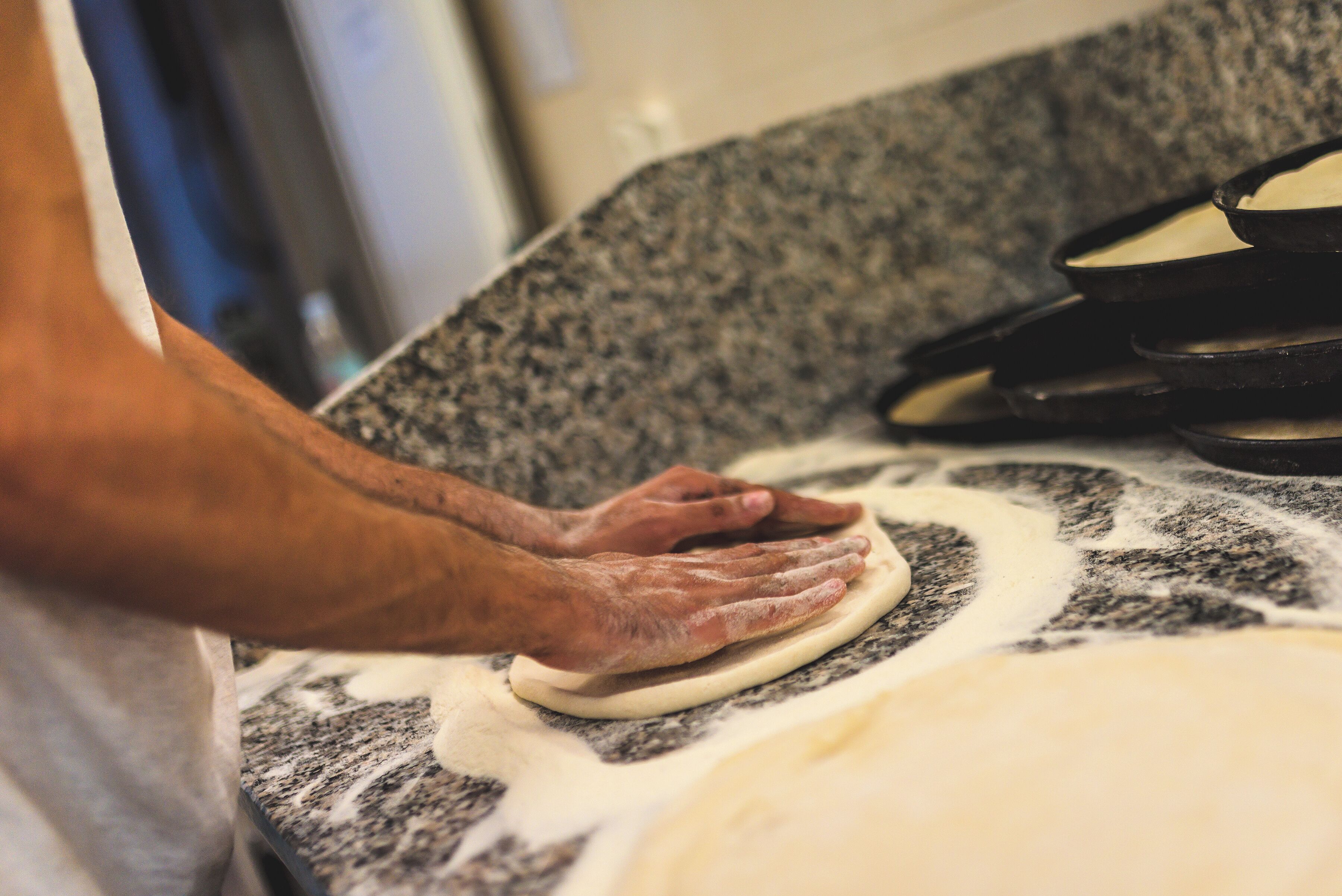 A person rolling dough on a granite countertop.