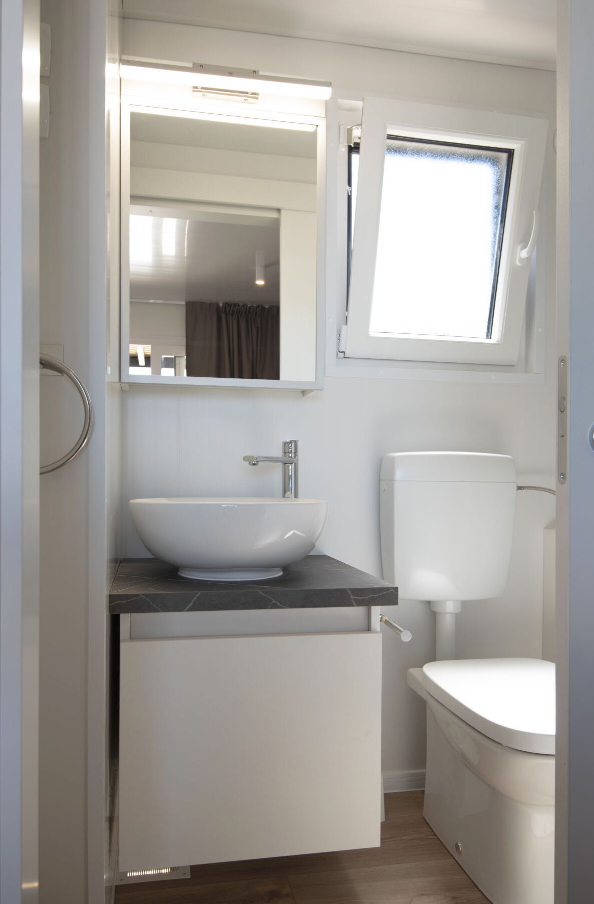 A compact bathroom with a white sink, a toilet, and a window above the toilet.