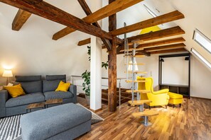 A loft-style room with exposed wooden beams, a gray sofa with yellow cushions, a yellow armchair, and a staircase.