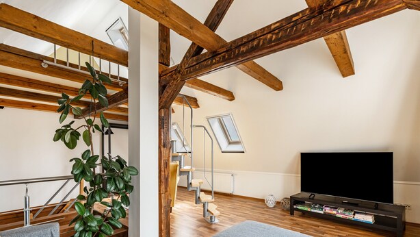 A loft-style room with exposed wooden beams, a staircase, a large window, a flat-screen TV, and a potted plant. - Holiday Home 'Oberlausitz With 160sqm' with Shared Terrace, Garden, and Wi-Fi (Cunewalde)