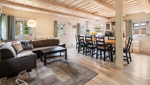 A spacious living area with a wooden ceiling, a sofa, a dining table with chairs, and a kitchen area. - Holiday Home 'Oberlausitz With 160sqm' with Shared Terrace, Garden, and Wi-Fi (Cunewalde)