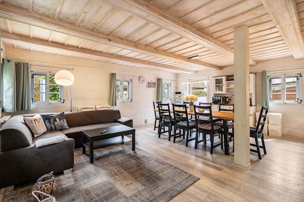 A spacious living area with a wooden ceiling, a sofa, a dining table with chairs, and a kitchen area.