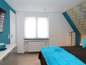 Une chambre à coucher avec un lit, une fenêtre, un radiateur, une porte blanche et un mur bleu.