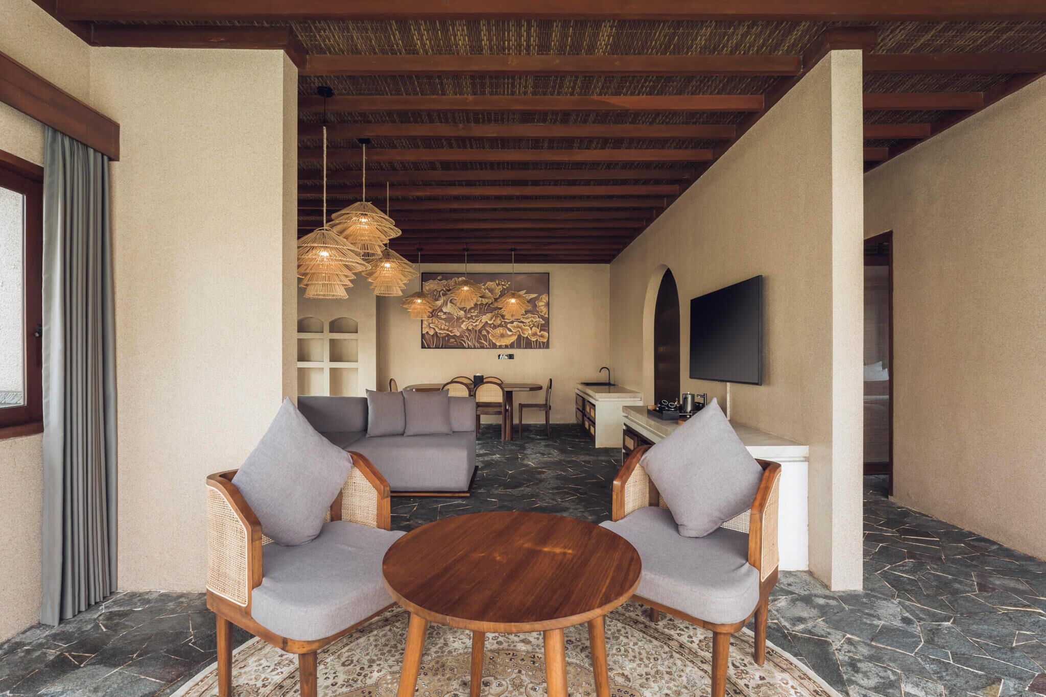 A modern living area with a sofa, two armchairs, a round wooden table, a TV, and a dining set.