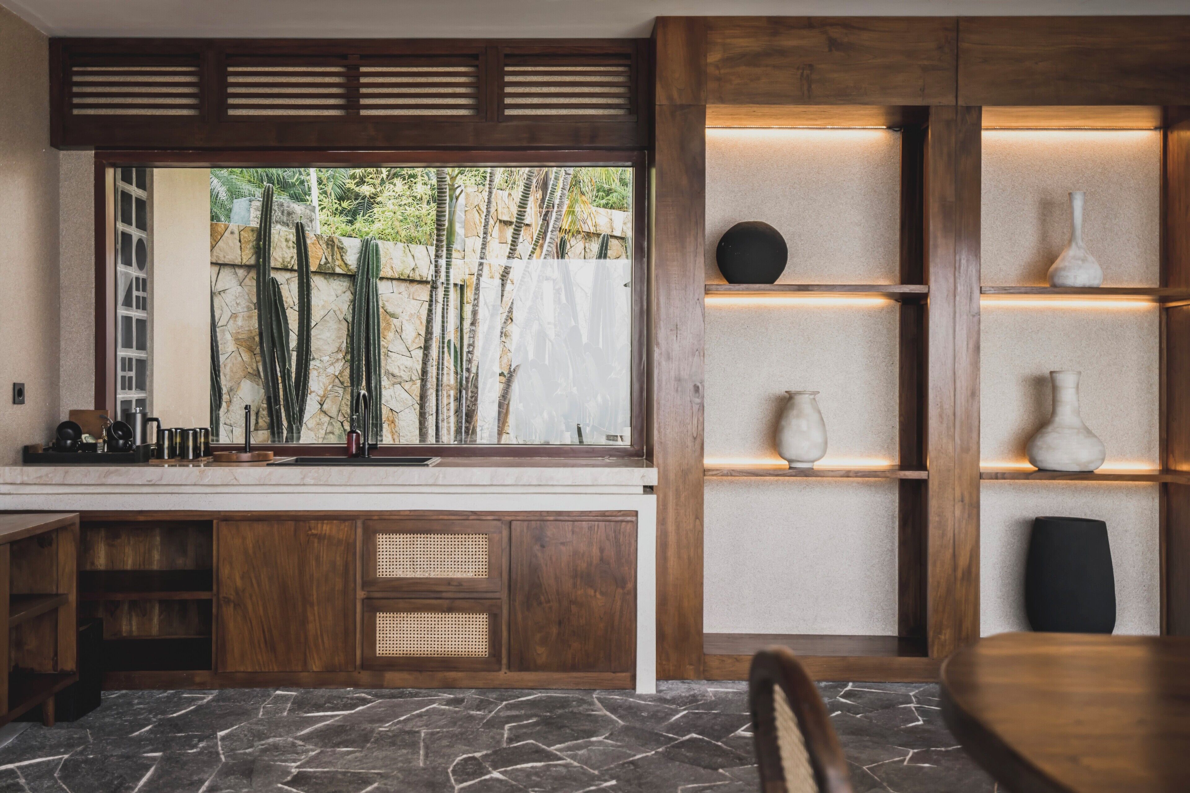 Una cocina moderna con encimera de piedra, armarios de madera y ventana con vistas a un jardín con cactus.