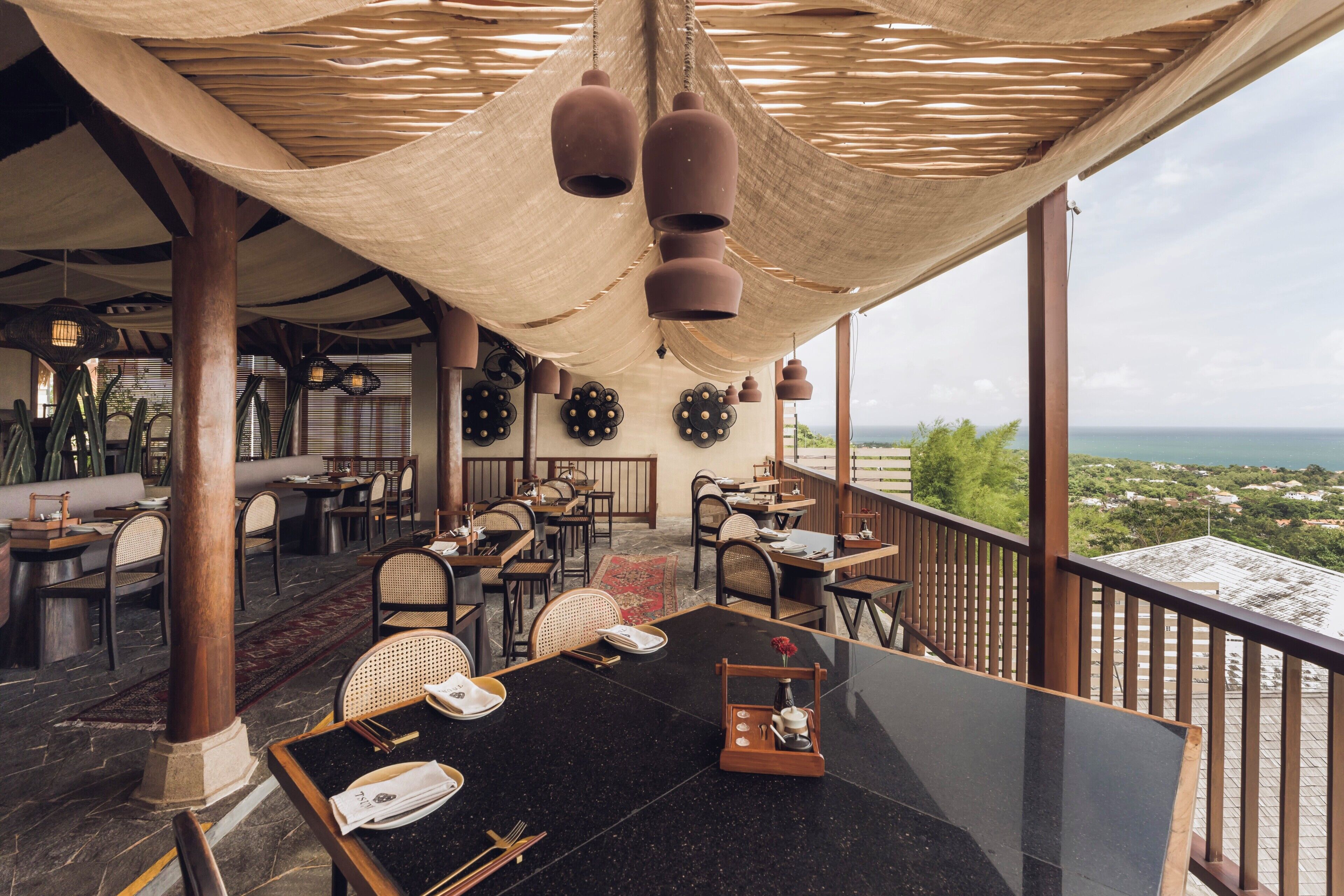Un restaurante con terraza, vistas al océano y techo de paja.