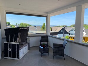 Un balcon agrémenté de meubles en osier, d’une plante en pot et offrant une vue sur des maisons et des arbres.