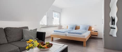 Une chambre à coucher moderne avec un lit, des tables de chevet, une commode, un canapé et une table basse sur laquelle se trouve un panier de fruits.