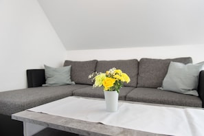 A modern living room with a grey sofa, a white vase with yellow flowers, and a white tablecloth.