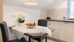 A modern kitchen with a dining table, chairs, a fruit bowl, a potted plant, and a hanging light fixture. - Apartment 'Birnau' with Lake View and Wi-Fi (Hagnau)