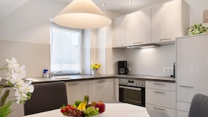 A modern kitchen with white cabinets, a dining table with a fruit bowl, and a window with a view. - Apartment 'Birnau' with Lake View and Wi-Fi (Hagnau)