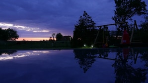 A calm outdoor area with a reflective water surface, trees, and a swing set.