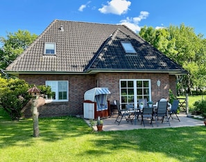 Une maison avec une façade en briques, un toit en tuiles, un patio couvert avec des meubles d’extérieur et un petit jardin.