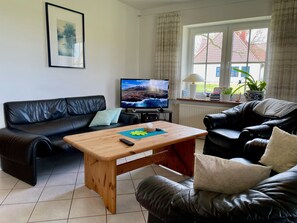 Un salon avec un canapé en cuir noir, une table basse en bois, un téléviseur et une fenêtre avec des rideaux.