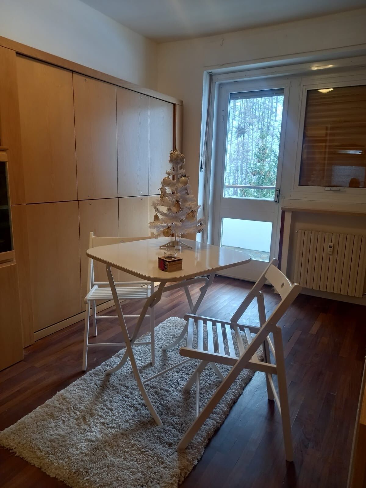 Et hyggeligt spiseområde med et hvidt bord, stole, en blød måtte og et lyst juletræ.