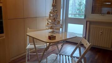 Et hyggeligt spiseområde med et hvidt bord, stole, en blød måtte og et lyst juletræ.