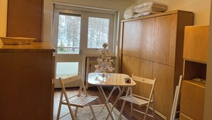 A compact room with a wooden cabinet, a small table with chairs, a radiator, and a window with a view of trees. - Carlotta whole apartment (Borgata Sestriere)