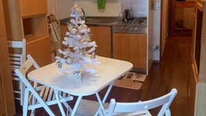 A compact kitchen with white cabinets, a dining table with white chairs, and a small white Christmas tree. - Carlotta whole apartment (Borgata Sestriere)