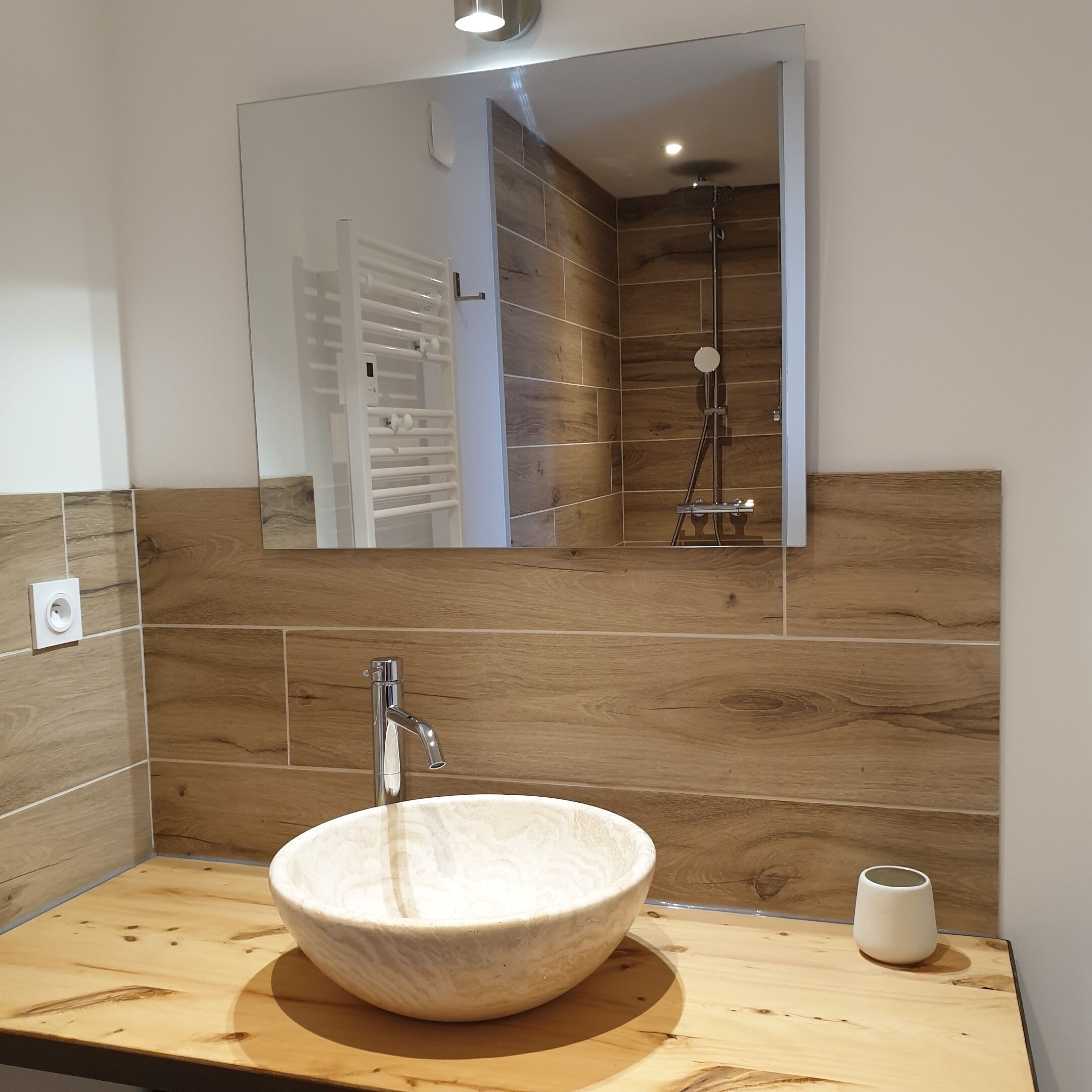 Un baño con tocador de madera, lavamanos blanco tipo lavabo y zona de ducha.