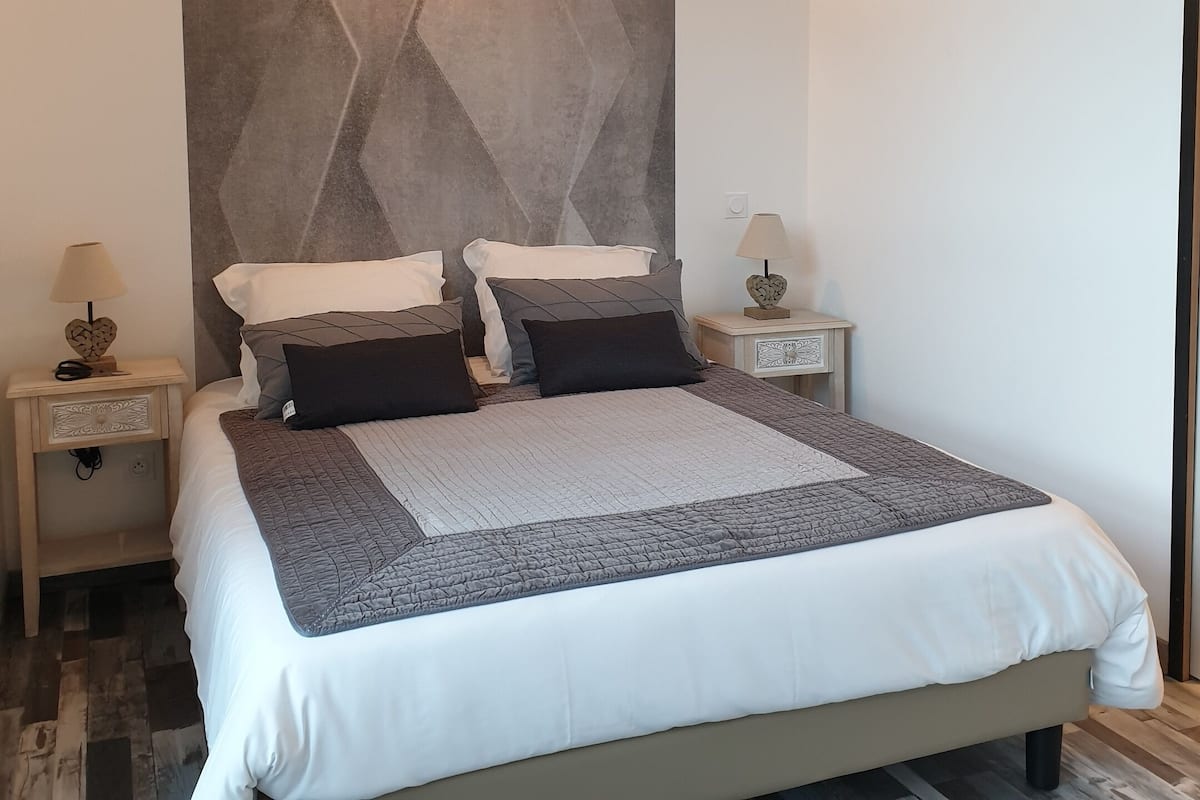 Une chambre moderne avec un grand lit, deux tables de chevet avec des lampes et un mur orné d’un motif géométrique.