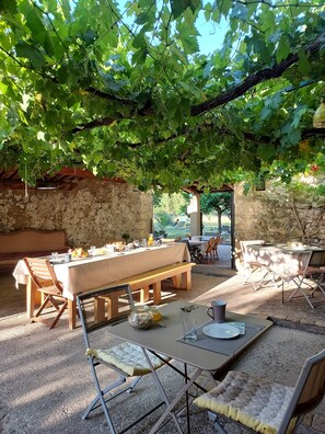 An outdoor dining area with rustic stone walls, wooden furniture, and a pergola covered with grapevines. - MAS DE REILHANETTE (Montbrun-les-Bains)