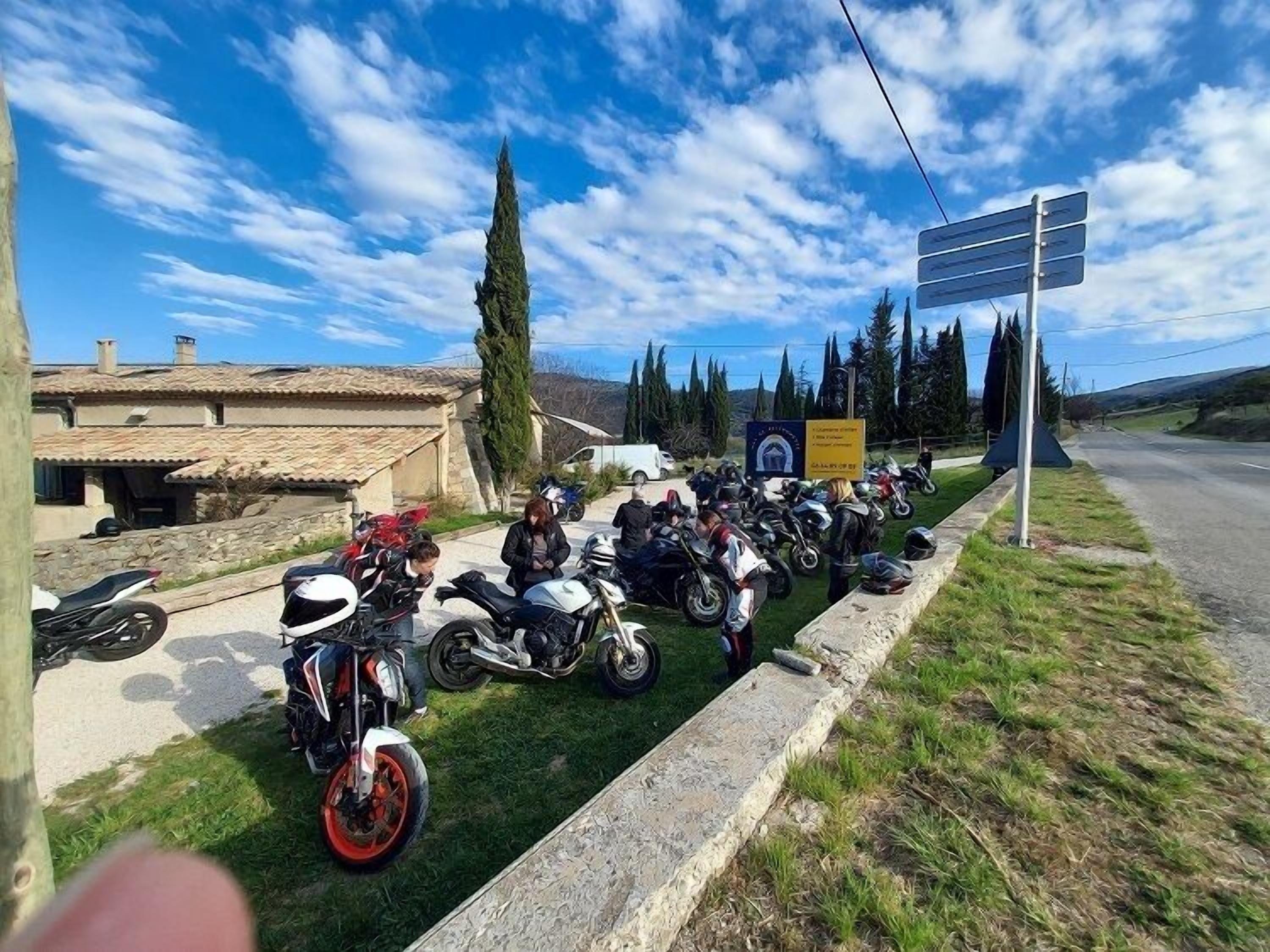 Een groep motorfietsen geparkeerd aan de kant van een grasrijk weggetje onder een heldere lucht.