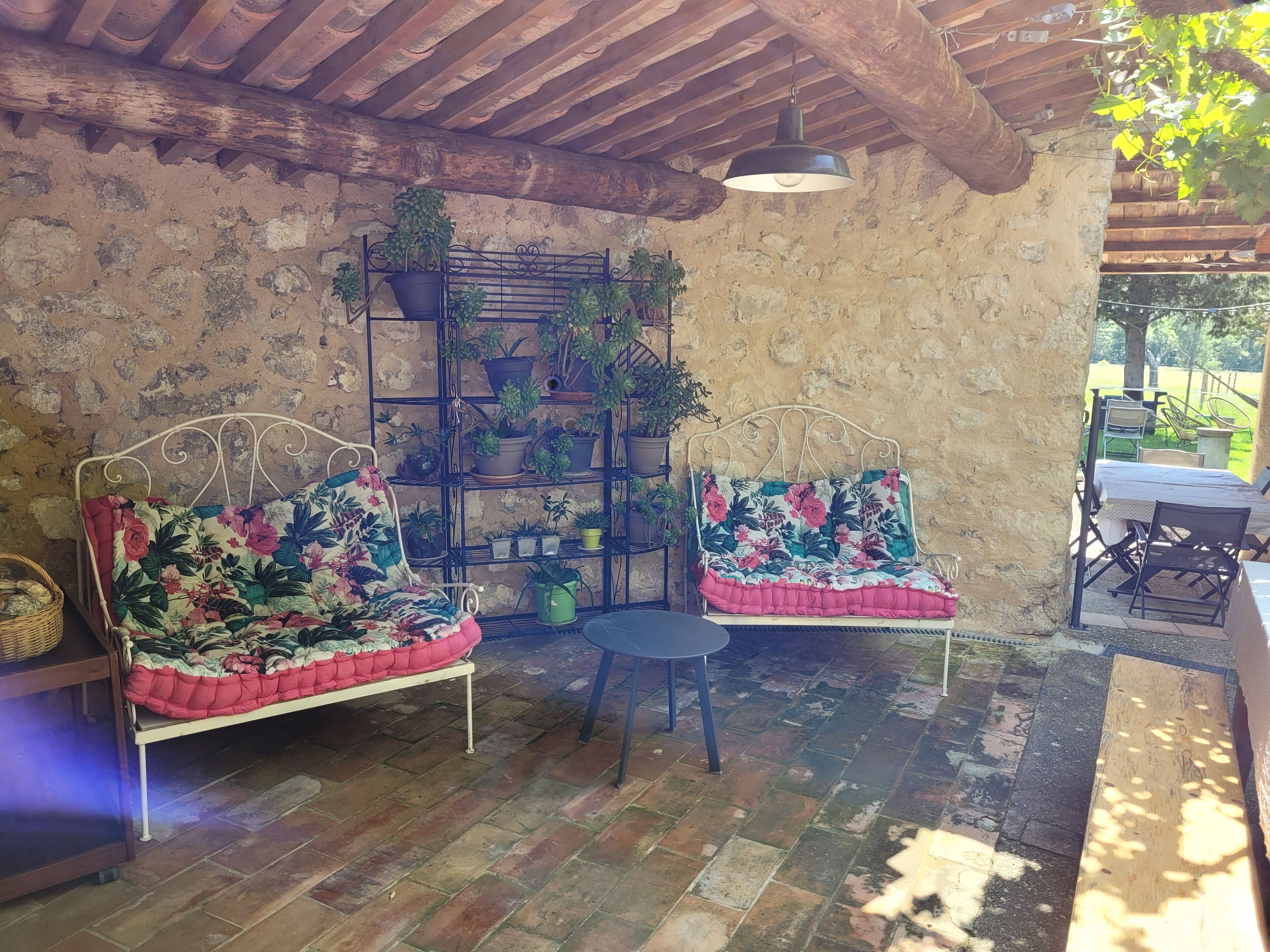 Un espace extérieur aménagé dans un style rustique, avec deux canapés à structure métallique, une petite table ronde et un présentoir métallique pour plantes en pot.