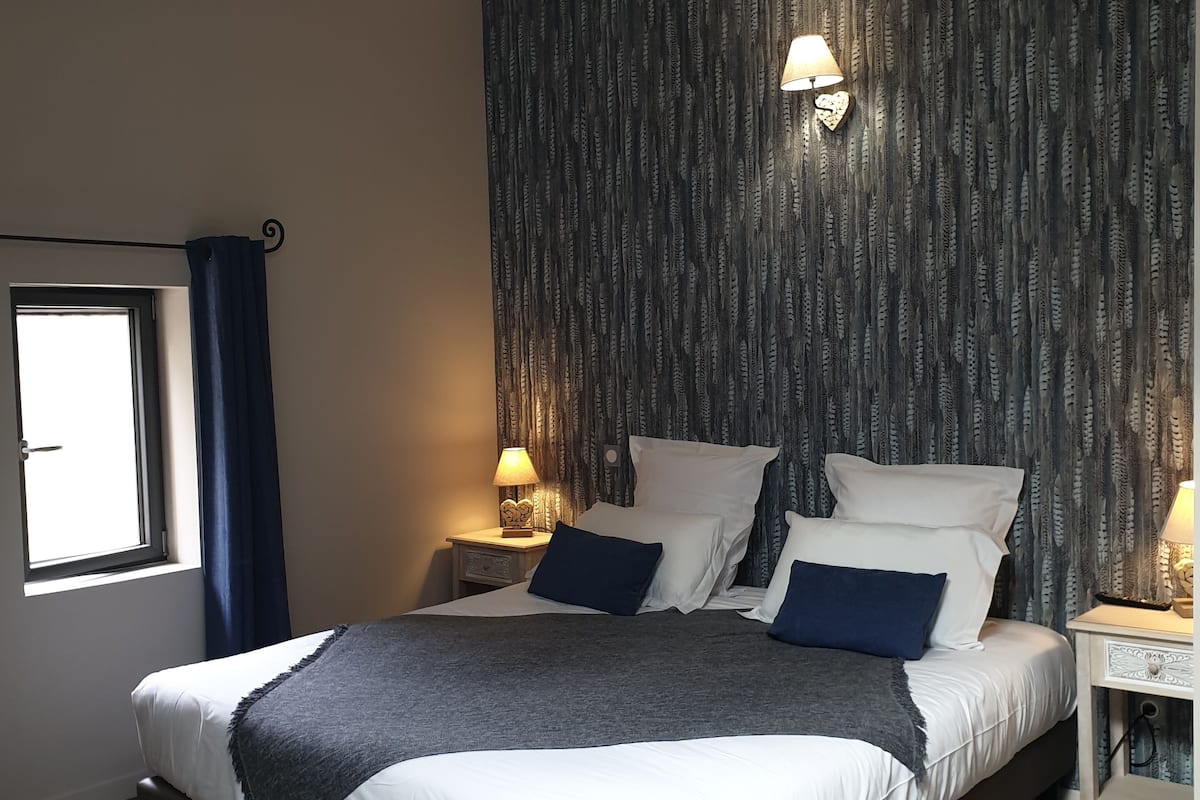 Une chambre avec un grand lit, deux tables de chevet, une fenêtre avec des rideaux et un mur décoré d’un motif.