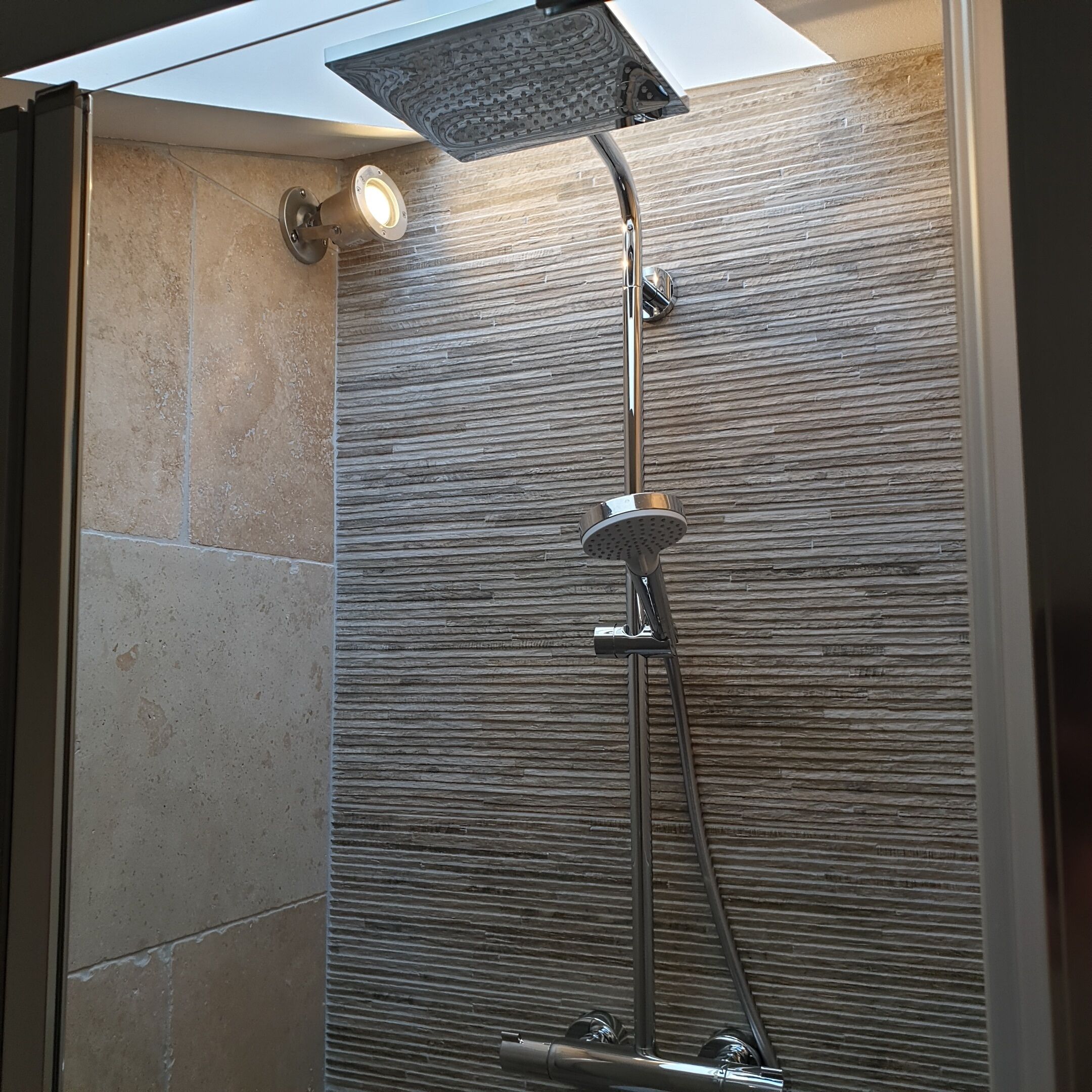 Une douche moderne dotée d’un pommeau de douche à pluie et d’un pommeau de douche à main, le tout fixé sur un mur texturé.