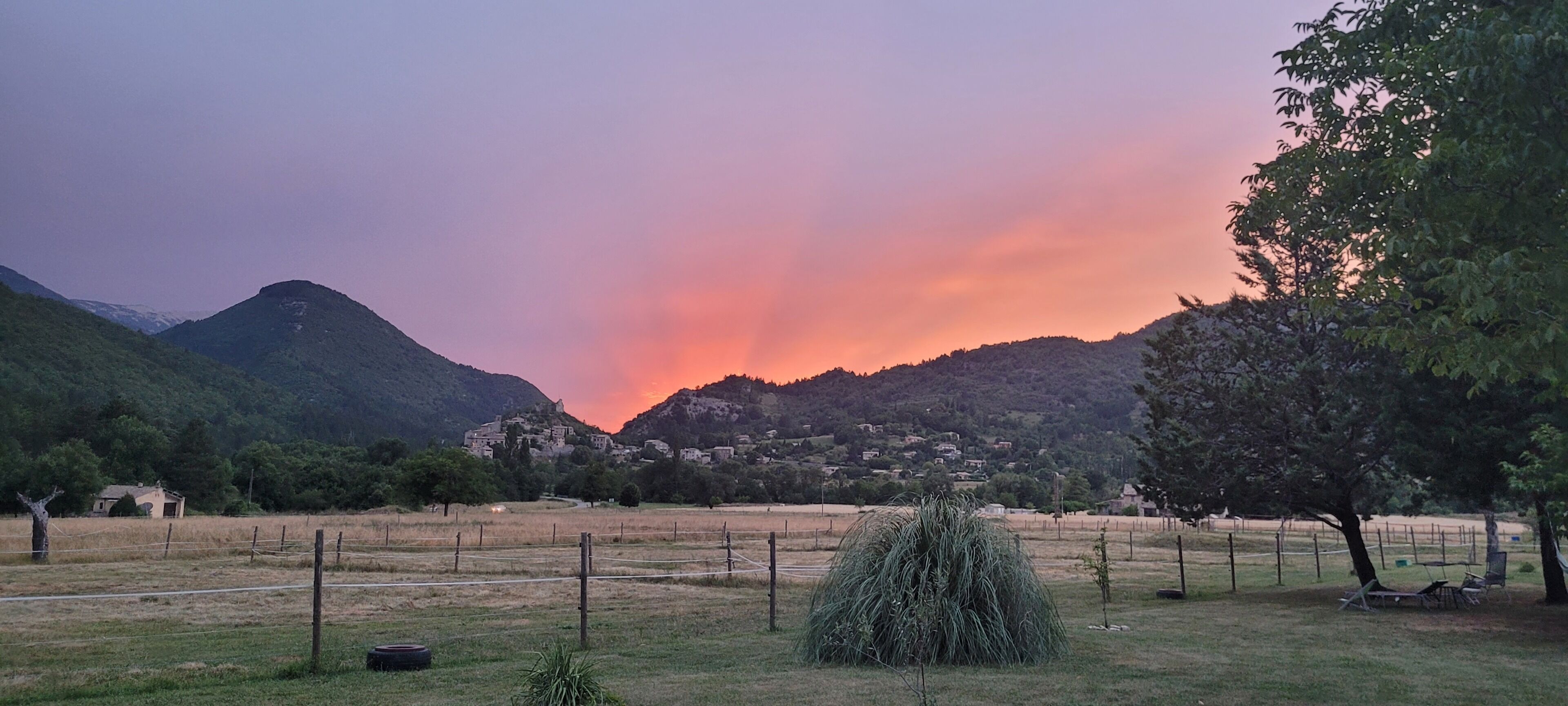 A rural landscape with a village nestled in the valley, surrounded by hills and a clear sky.