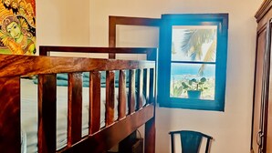 Una escalera con barandilla de madera, una ventana con marco azul que da a la playa, y una planta en maceta en el alféizar.