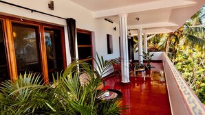 Un espacio al aire libre techado con suelo rojo, columnas blancas y abundante follaje.