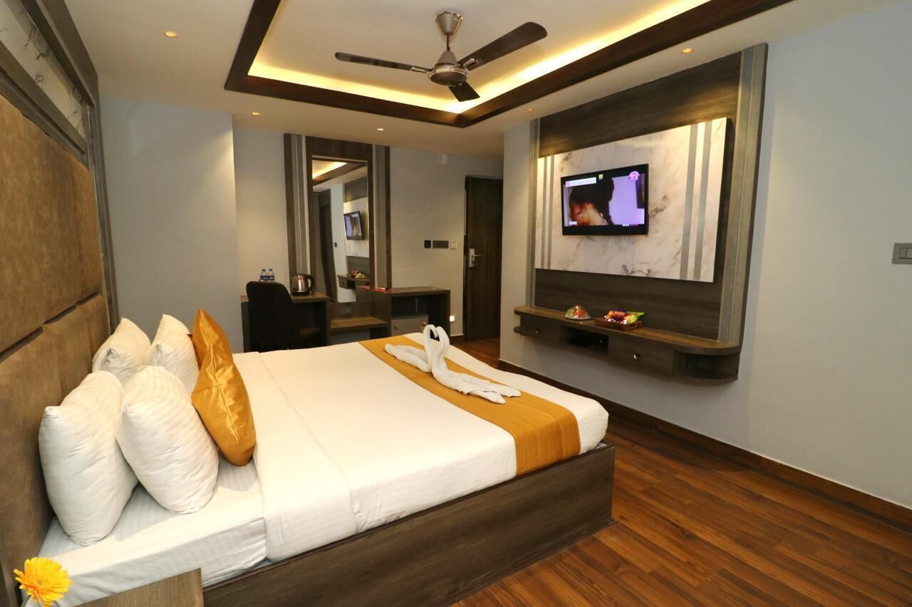 A modern hotel room with a large bed, a television mounted on the wall, and a ceiling fan.