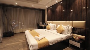 A modern hotel room with a large bed, a bedside table with a fruit bowl, and a view of the city at night. - Transitel A Boutique Hotel (Barasat)