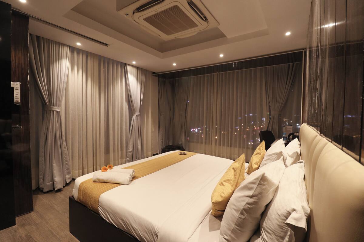 A modern hotel room with a large bed, a view of the city at night, and a large window with curtains.