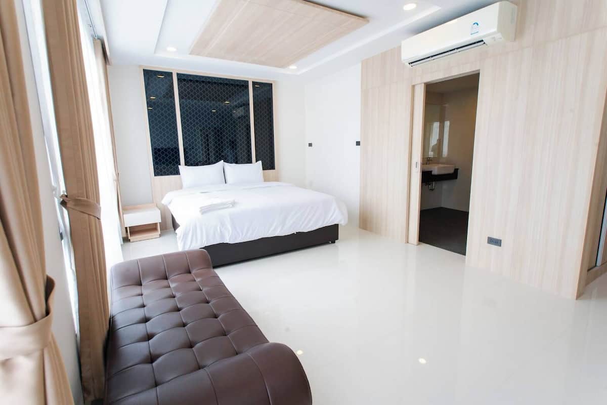 Ein modernes Schlafzimmer mit einem großen Bett, einer Sitzecke und einem durchgehenden Türrahmen sichtbaren Badezimmer.