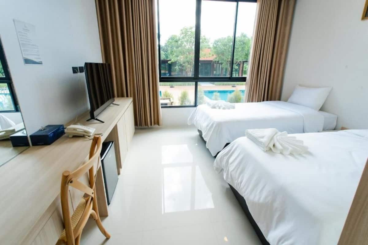 Ein Hotelzimmer mit zwei Betten, einem Schreibtisch mit Computer und Telefon, einem Fernseher und Blick auf einen Swimmingpool.