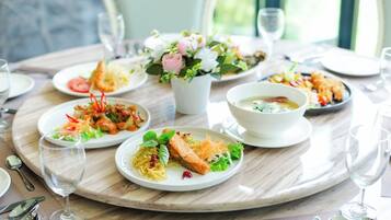 A dining table with plates of food, glasses, and a vase of flowers.