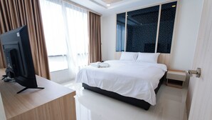 Een hotelkamer met een groot bed, een televisie op een bureau en een raam met gordijnen.