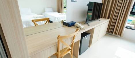A hotel room with a wooden desk, two single beds, a television, and a small trash bin.