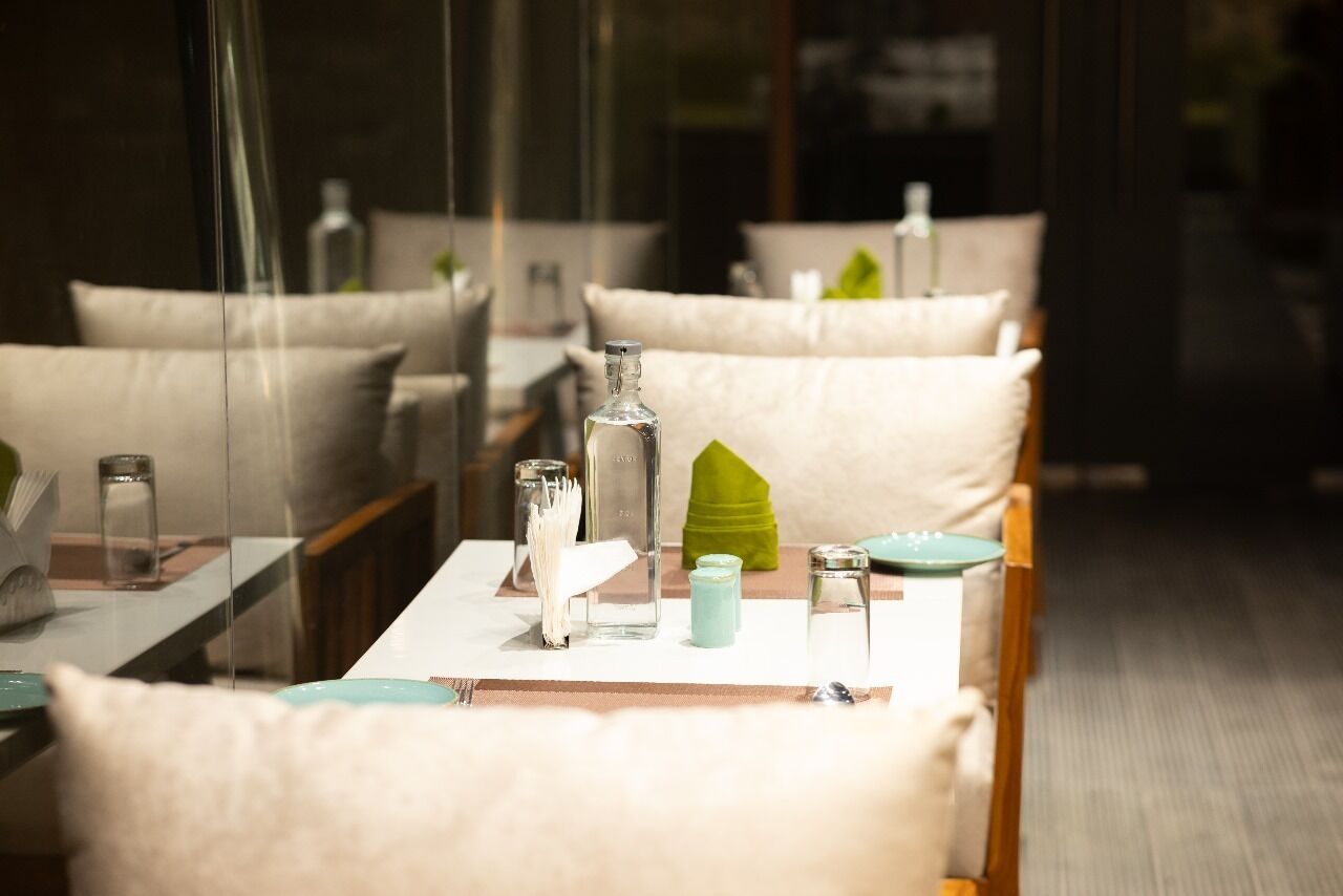 A dining area with tables set for two, featuring glassware, napkins, and a green decorative item.