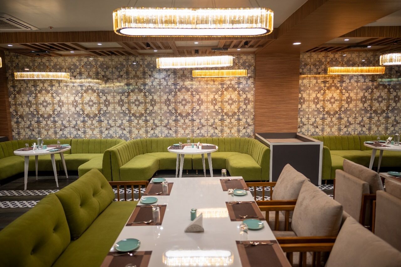 Un restaurante con asientos tapizados en verde, mesas redondas blancas y un fondo de papel tapiz estampado.