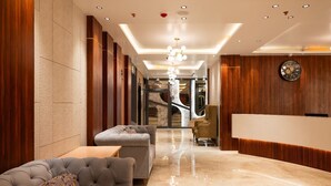 A modern lobby with a plush sofa, a reception desk, and a chandelier. - The Grand Royal Hotel (Samastipur)