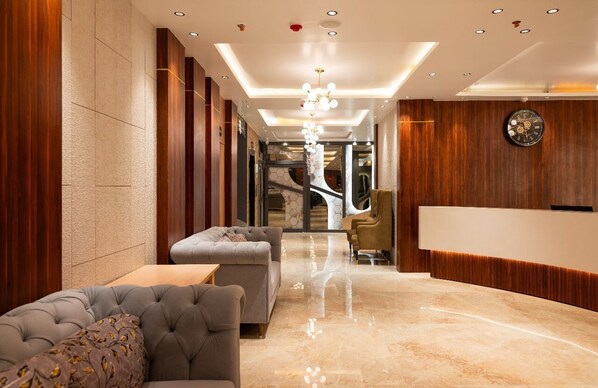 A modern lobby with a plush sofa, a reception desk, and a chandelier.