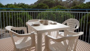 Un balcón con mesa y sillas, barandilla y vista a árboles.